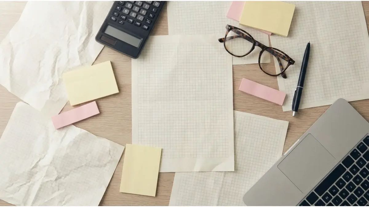 Bureau couvert de feuilles quadrillees, calculatrice et post-it illustrant le travail manuel autour d un logiciel